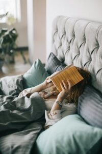 Woman resting in bed holding a book, creating a serene indoor atmosphere perfect for relaxation and leisure.